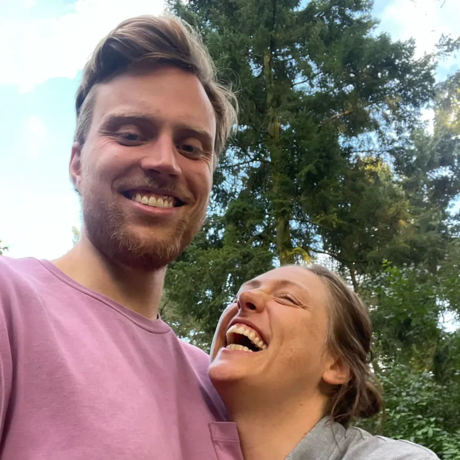Teresa und Markus lachen in die Kamera, draußen zwischen Bäumen